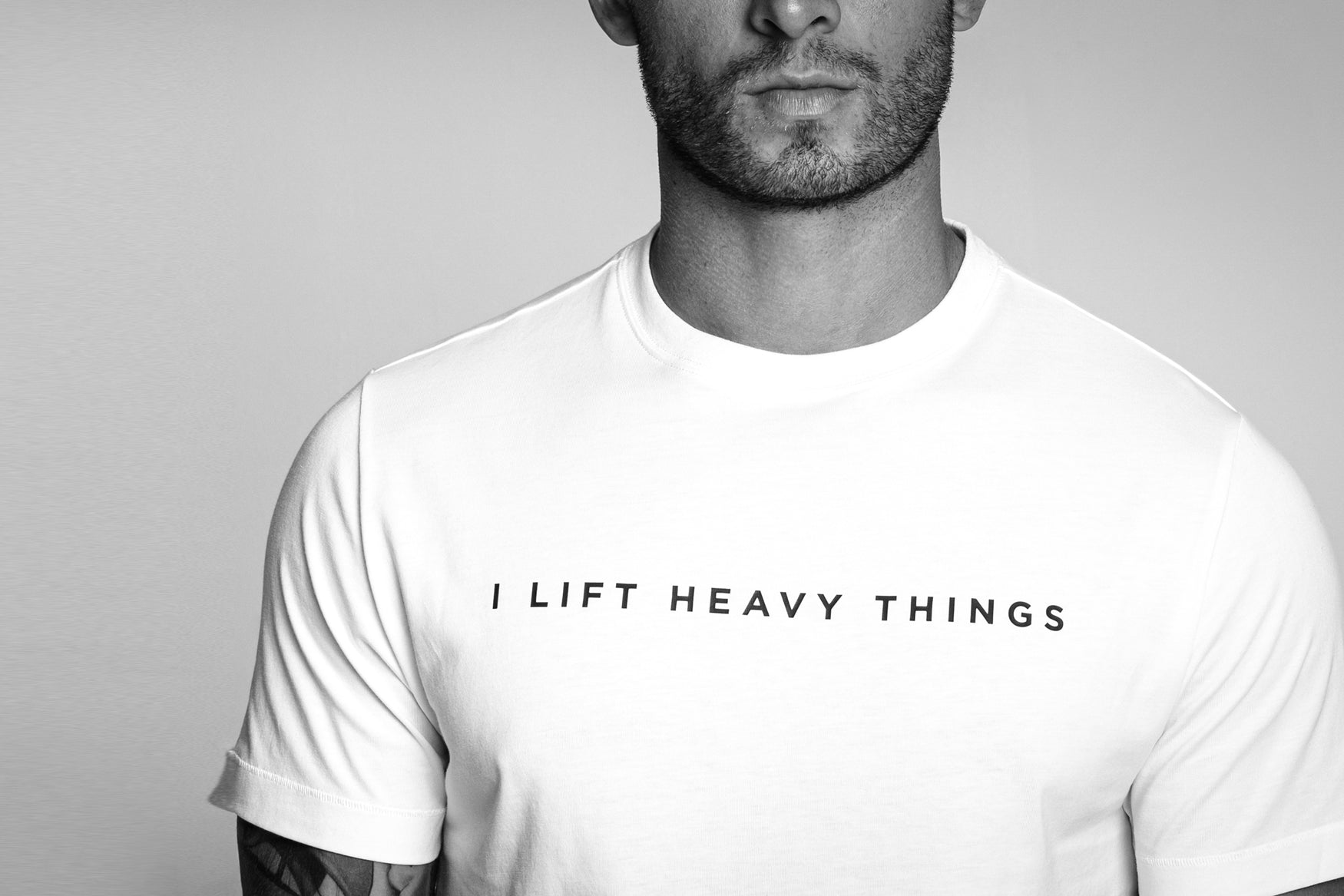 A man wearing a white t-shirt with the words I lIft Heavy Things printed across the front